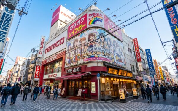 Bustling Tokyo street featuring vibrant storefronts, including Namco and Gundam Base, attracting crowds of anime enthusiasts.