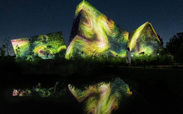 Vibrant light projections dance across modern architecture at night, captivating viewers with artistic brilliance and reflections at teamLab Botanical Garden Osaka