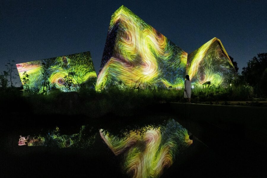 Vibrant light projections dance across modern architecture at night, captivating viewers with artistic brilliance and reflections at teamLab Botanical Garden Osaka