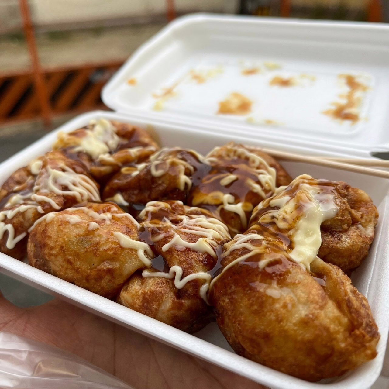 Delicious takoyaki balls drizzled with savory sauce and mayo, served in a takeout container, perfect for a flavorful snack.