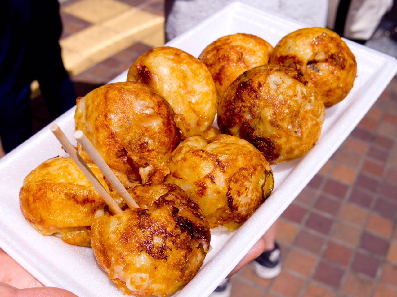 Warm and crispy takoyaki balls served on a styrofoam tray, showcasing a popular Japanese street food delight.
