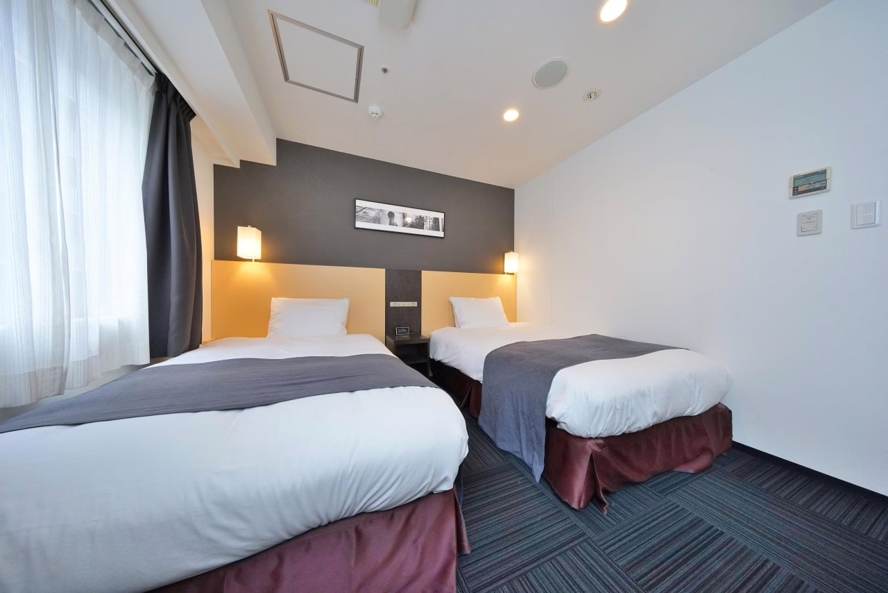 Cozy hotel room featuring two neatly made beds, modern decor, and soft natural light from the window, perfect for relaxation.