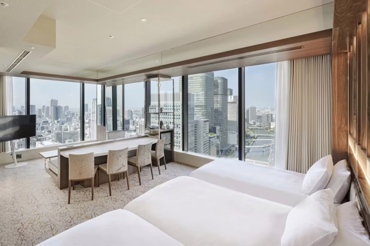 Modern hotel room with twin beds, a sleek workspace, and panoramic city views, perfect for business or leisure travel.