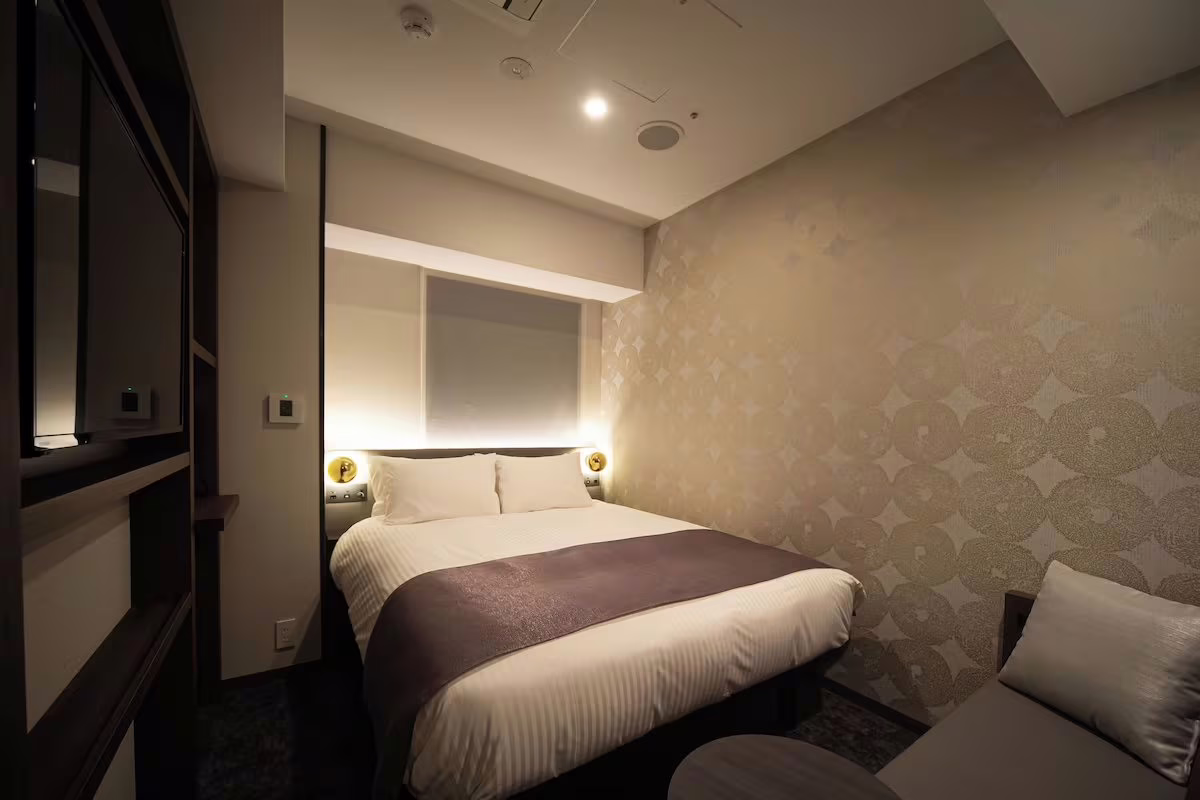 Cozy hotel room featuring a comfortable double bed, modern decor, ambient lighting, and a sleek seating area.