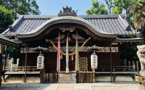 Shinto shrine entrance adorned with traditional lanterns and ceremonial ropes, surrounded by lush greenery and stone lion statues.