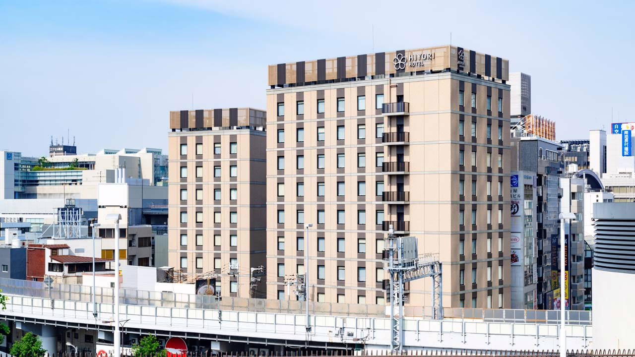 Modern Hiyori Hotel stands among urban buildings, representing contemporary hospitality in a bustling cityscape.