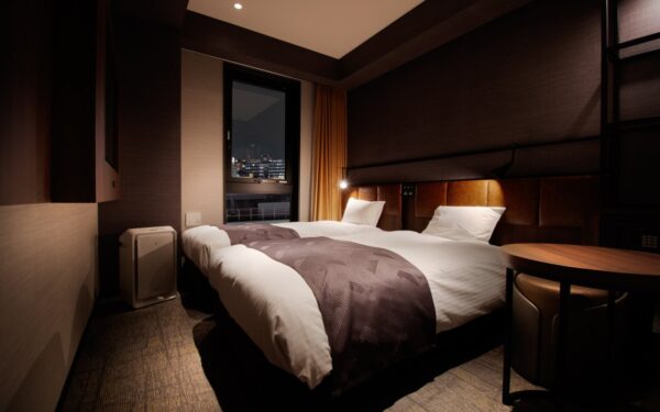 Cozy hotel room with two beds, warm lighting, and a city view through the window, perfect for travelers seeking comfort.