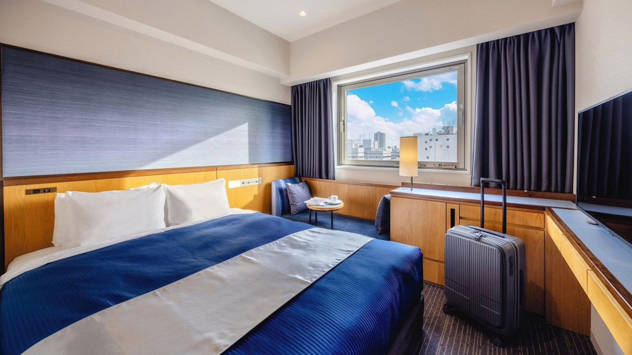 Modern hotel room with a king-sized bed, city view, and cozy seating area, ideal for travelers seeking comfort and style.