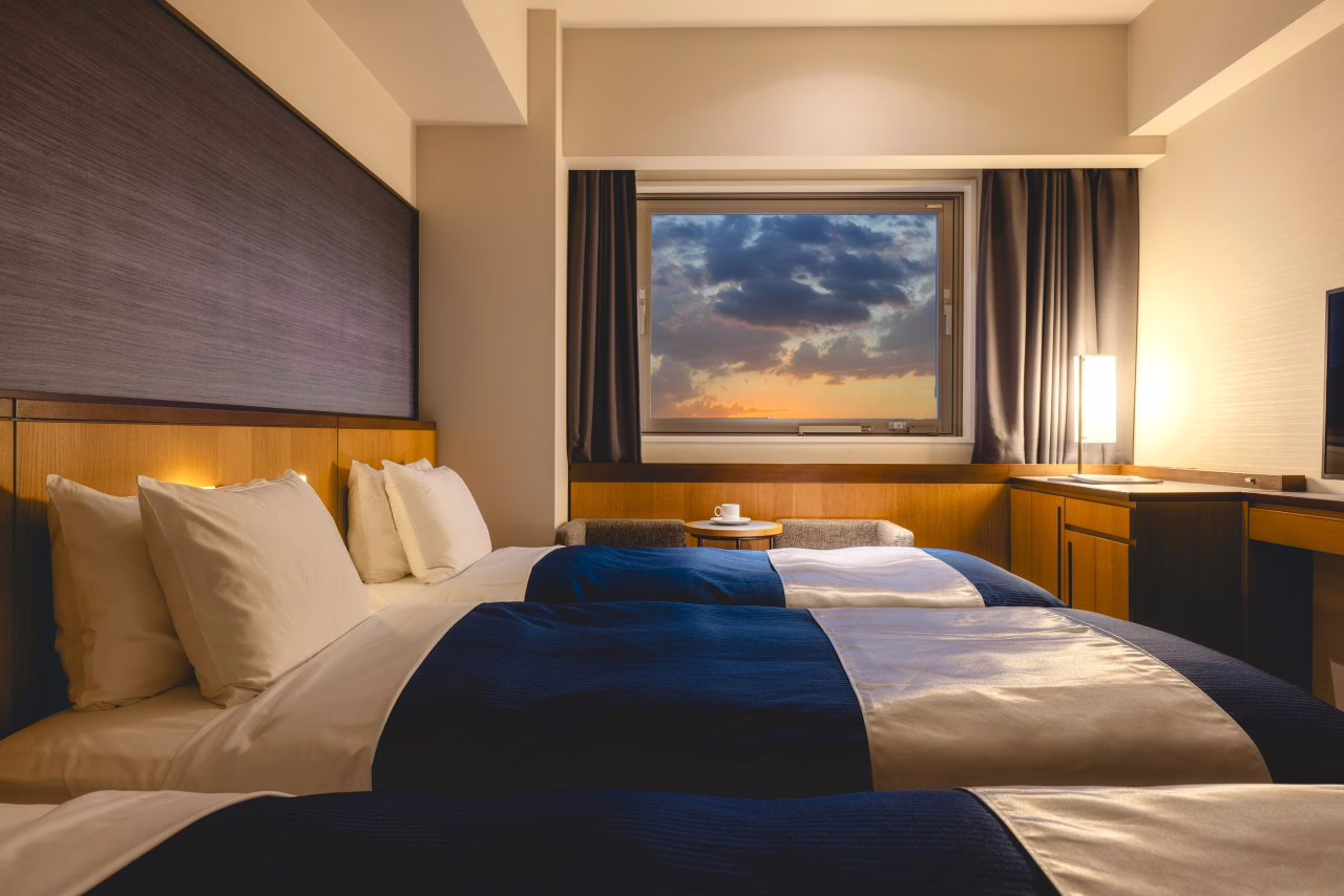 Cozy hotel room with two beds, overlooking a serene sunset through a large window, ideal for relaxing getaways.