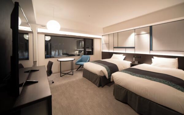Modern hotel room featuring two beds, minimalist design elements, and a cozy seating area with natural light streaming in.