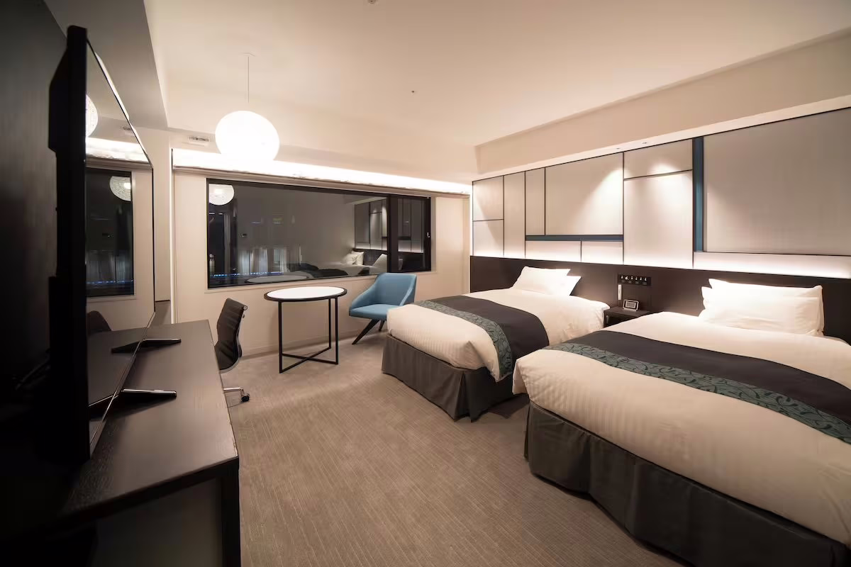 Modern hotel room featuring two beds, minimalist design elements, and a cozy seating area with natural light streaming in.