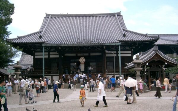 Crowds visiting a traditional Japanese temple, enjoying the serene environment and cultural heritage on a sunny day.