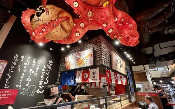 Vibrant restaurant interior with an octopus lantern and chefs preparing traditional Japanese cuisine in a lively atmosphere.