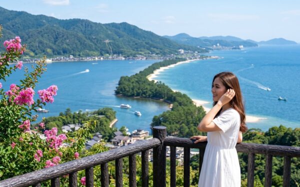 Kannaya Nareswari enjoying a scenic view of a coastal landscape with lush mountains and vibrant flowers, perfect for travel inspiration.