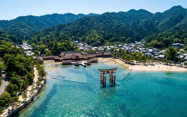 The iconic red torii gate stands majestically in the clear waters, symbolizing traditional Japanese spirituality against a serene landscape.
